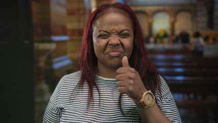 Woman showing thumbs up in a historic church interior with wooden pews stained glass windows and brick columns; approval.