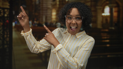 Young african american woman points finger upward toward altar inside church building smiling...