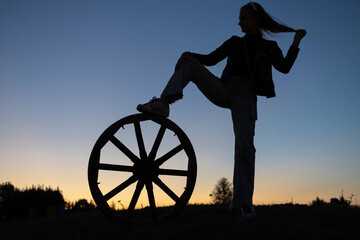 Interesting silhouette confident woman standing at sunset against sky, putting one foot on big...