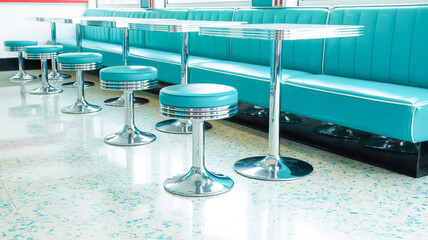 A retro-style diner interior with turquoise leather banquette seating along a white wall.