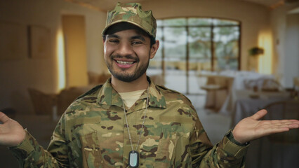 Man in camouflage uniform wearing dogtags spreads open palms in restaurant building with large...