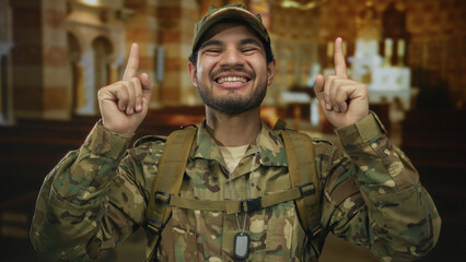 Man in camouflage uniform with dog tag smiling while pointing finger up in wooden pews of church;...