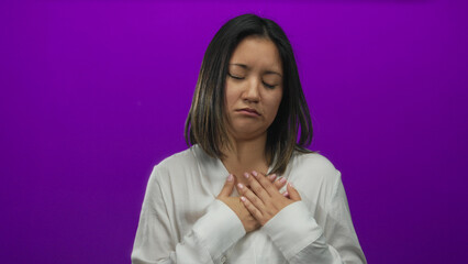 Woman feeling emotional with hands on chest against a vivid purple background, expressing serene...
