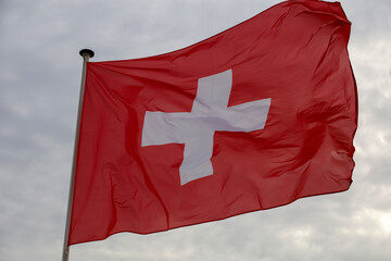 The Swiss flag flutters in the wind against a cloudy sky