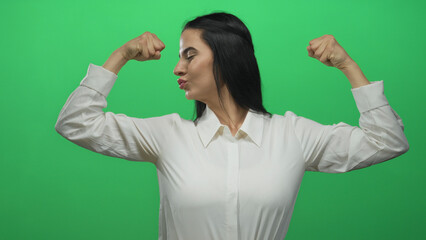 Hispanic woman in white shirt celebrates with arms raised against a green wall, expressing joy and...