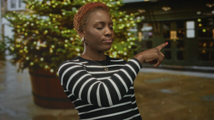 Young african american woman wearing striped sweater pointing finger on city street; highlight...