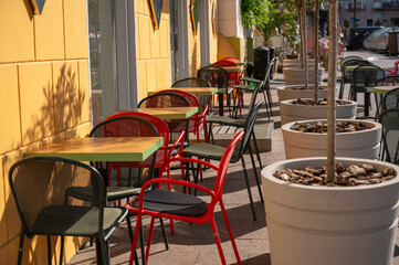 Street cafe tables with bright red, yellow and green furniture and plants in big pots