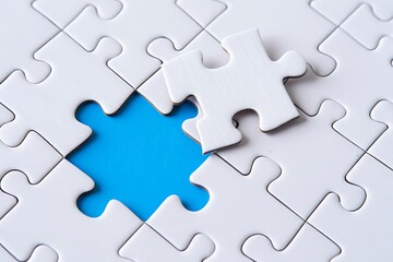 A single white puzzle piece is missing from a completed jigsaw puzzle revealing a vibrant blue background symbolizing a missing element or a solution
