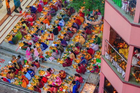 Dhaka, Bangladesh - 13 November 2018: Aerial view of a vibrant gathering, women in colorful saris sit on steps, surrounded by glowing candles and offerings.