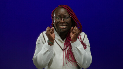 Woman with red braids and glasses looking anxious in front of an isolated blue background, expressing worry or concern.