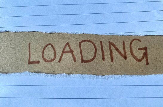 Handwritten word Loading is displayed on a brown background, positioned between two torn lined notebook paper. The concept of waiting or a state of being in progress, often associated with technology.