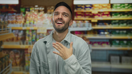 Young hispanic man in grocery store expressing emotions surrounded by various colorful products on...