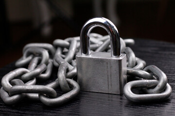Silver padlock and iron chain on dark background.