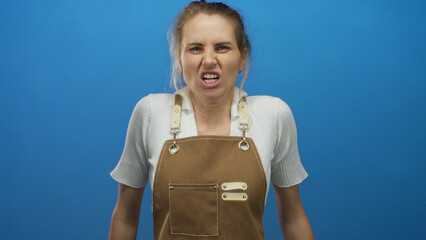 Woman shouting wearing apron against blue background displaying strong emotion and passion