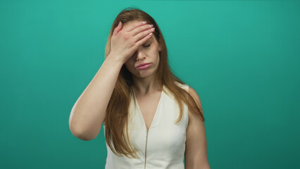 Young woman in white sleeveless top with long brown hair holding palm to forehead in studio; stress.