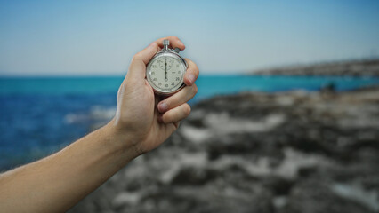 Man holding stopwatch on a scenic seaside beach with a clear blue sky, illustrating precision and...