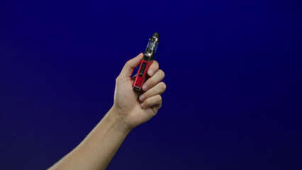 Man holding a vape device with a red design set against a blue isolated background, showcasing...
