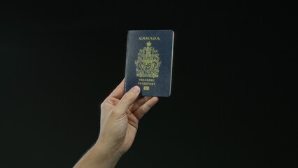 Male hand holding canadian passport against a black background highlighting travel identity concept with isolation.