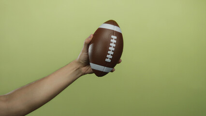 Male hand holding a football set against a yellow background, showcasing the sport equipment in a...