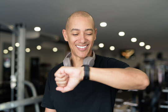 Hispanic bald man athlete in gym using smartwatch fitness tracker