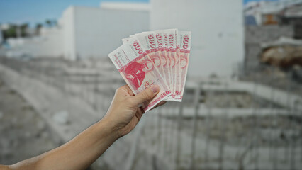 Male hand holding icelandic krona banknotes at a construction site, highlighting financial...