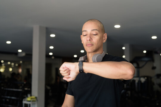 Hispanic bald man athlete in gym using smartwatch fitness tracker