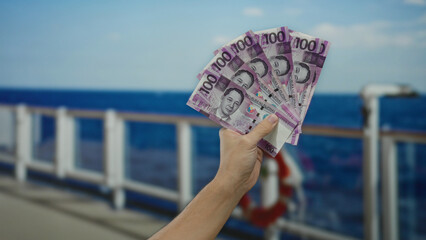 Man holding philippine pesos on a cruise ship with a scenic seaside view, showcasing outdoor travel...
