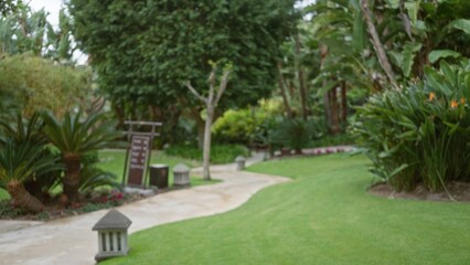 Fototapeta premium Blurred view of a tropical resort garden featuring lush greenery, winding paths, and ambient lighting in a luxury outdoor setting with defocused trees and bokeh effect.
