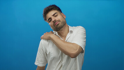 Hispanic young man with hand on shoulder in studio wearing white linen shirt and trimmed beard;...