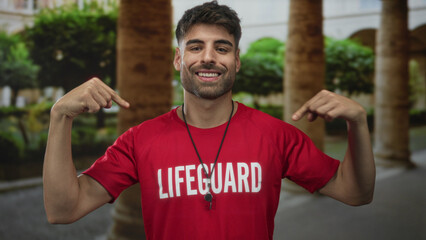 Lifeguard man wearing red shirt and whistle around neck points finger to chest in building...