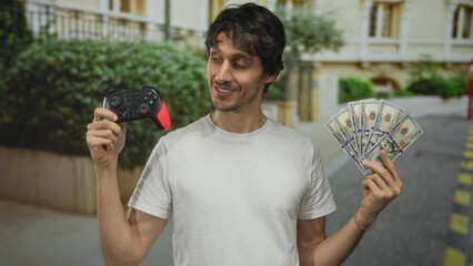 Man holding gaming controller in one hand and fanned cash with other hand on city street; winning...