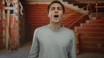 Young hispanic man wearing a gray sweater gesturing energetically indoors at a construction site...