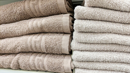 Several stacks of soft, neutral-colored towels in shades of beige and gray, neatly folded and...