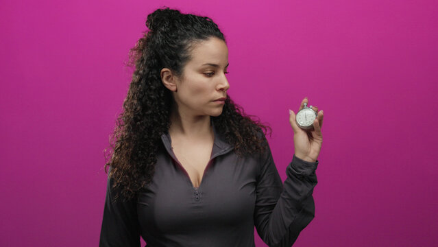 Woman holding stopwatch against pink background in isolation suggesting time management and focus with youthful energy and hispanic descent expression.