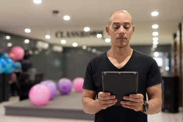Hispanic bald man athlete in gym classroom using digital tablet computer