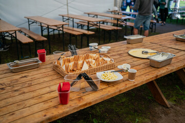 Outdoor buffet table with sliced white bread, butter, cheese and condiments under event tent with wooden benches prepared for group meal at countryside festival or catering event