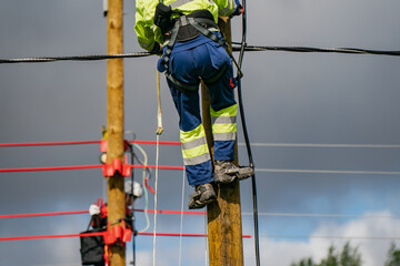 Electrical lineman climbing wooden utility pole with safety harness and protective equipment during...