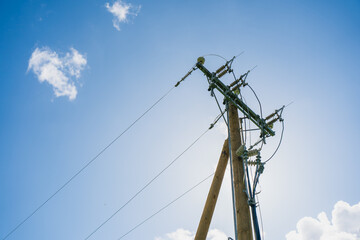 Wooden utility pole with electrical power lines and insulators against blue sky with clouds in...