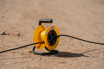 Yellow portable cable reel with black electrical cord extended on gravel ground for outdoor...