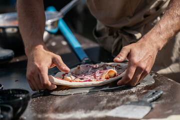Chef hands shaping raw pizza with tomato sauce ham onion and cheese on peel before placing in oven showing traditional homemade cooking italian cuisine and street food preparation
