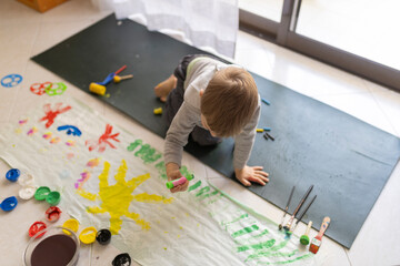 Child painting on floor with colorful tempera colors and brushes