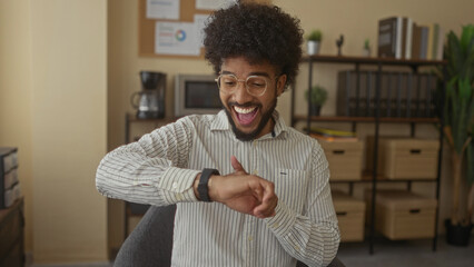 Man checking smartwatch in modern office, exhibiting enthusiasm, surrounded by bookshelves and...