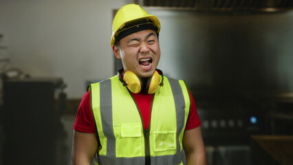 Construction worker smiling indoor wearing safety helmet and vest in industrial setting with...