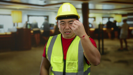 Man wearing construction outfit in hotel lobby with determined look amidst busy indoor environment