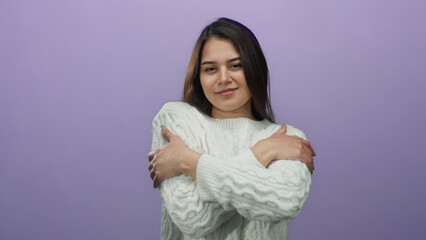 Woman smiling warmly in cozy white sweater embracing herself against vibrant purple backdrop...