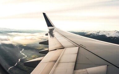 Airplane wing over mountains and clouds at sunrise, aerial view