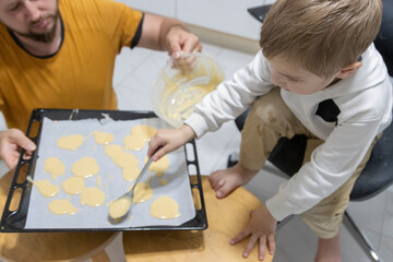 Father and son preparing cookies on baking sheet in kitchen