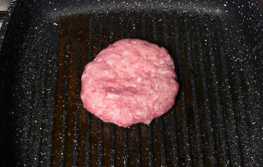 Raw burger cooking in a hot grill pan