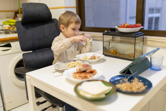 Child eating lunch at home with fish tank and tablet - Powered by Adobe