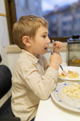 Blond boy eating pasta with ham and cheese at home